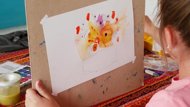 Little girl with pigtails learns to paint with watercolor paints. draws flowers