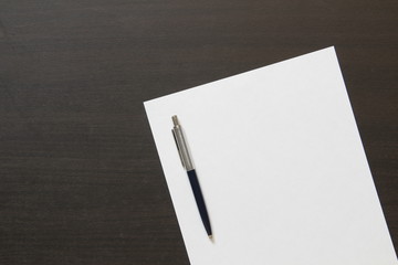 Template of white paper with pen on dark wenge color wooden background.
