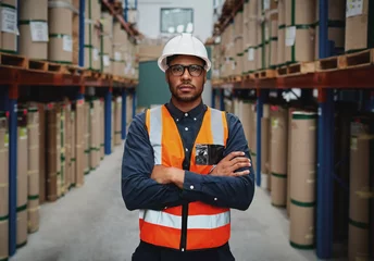Foto op Canvas Confident young manager with arms crossed standing wearing orange vest and white hardhat in manufacturing unit looking at camera © StratfordProductions