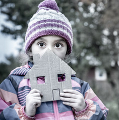 The girl is five years old. She is holding a house cut out of cardboard.