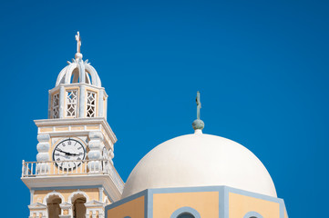 Colorful church dome matching the baroque yellow and gray coloring of the clock tower of St John the Baptist Cathedral in the village of Fira, Santorini, Greece