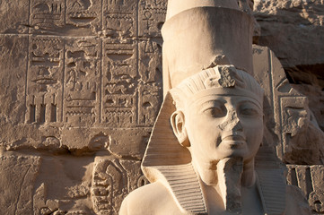 Close-up of the stone face of the ancient Egyptian pharaoh Ramses II in front of a wall of...