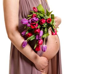 Pregnancy. Pregnant woman holding tulips in her hands near her bare belly