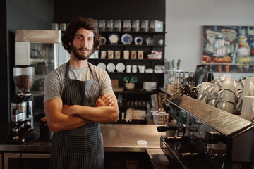 Male business owner behind the counter of a coffee shop with folded hands looking at camera