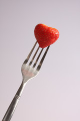 A studio photograph of a fresh strawberry and a fork against a white background