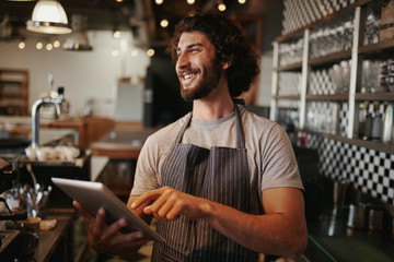 Portrait of successful young caucasian cafe owner standing behind counter using digital tablet