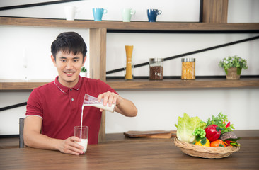 Asian syoung man with casual  red t-shirt enjoy having breakfast, drinking milk. Young man cooking food  in the loft style kitchen room