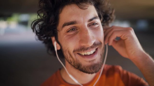 Cheerful young man inserting the white earphones in his ears foe listening motivational music