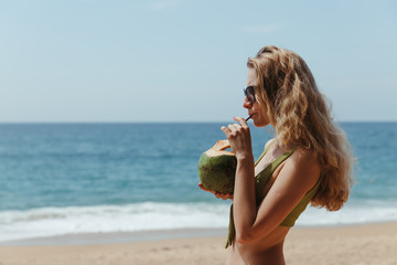 The girl with the coconut on the beach. Girl drinks coconut milk on the beach. High quality photo