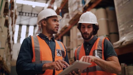 Diverse young male workers discussing and using digital tablet while supervising production at distribution warehouse - Powered by Adobe