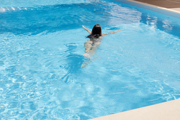 Dark haired woman with swimsuit swimming on blue water pool at luxury spa salon or in hotel,...