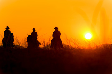 Obraz na płótnie Canvas Cowboy riding a horse carrying a gun in sunset with mountain 