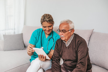 Health visitor and a senior man during home visit. A female nurse or a doctor showing test results on a tablet. Senior patient and caregiver using tablet. I found some entertainment for you