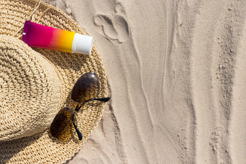 A bottle of sunscreen with sunglasses and panama hat  on a beach, summer skin remedies and...