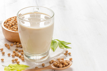 Soy or soya milk in a glass with soybeans in wooden bowl background