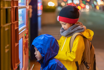 Two children is choosing drinks from Japanese Vending machine near Sendai station at night.