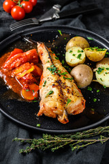 Cooking in tomatoes monkfish fish with baked potatoes. Fresh seafood. Black background. Top view