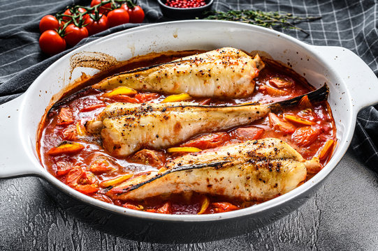 Cooking in tomatoes monkfish fish in a baking dish. Fresh seafood. Gray background. Top view