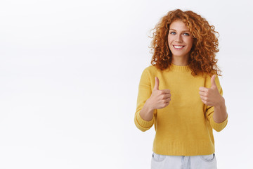 Cheerful attractive curly ginger woman in yellow sweater show thumbs-up in approval, cheering or...