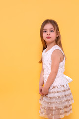Shot of a  little  serious girl with long blonde hair  against yellow background with copy space in studio