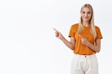 Confident, sassy good-looking modern blond female in orange t-shirt, pants, pointing fingers left...