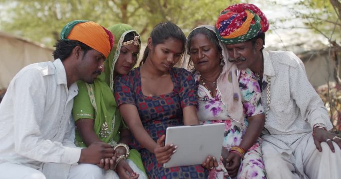 Three generations of a Rajasthani family, in traditional colorful costumes in India taking photo video selfies on a portable wifi tablet with touch screen in a rural setting exterior outdoors house