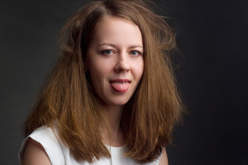 Fototapeta premium Studio portrait of a blonde in a white blouse on a black background. playing the fool, hanging out tongue