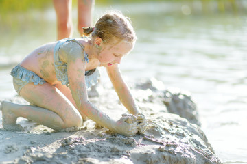 Young girl taking healing mud baths on lake Gela near Vilnius, Lithuania. Child having fun with mud. Kid playing with clay.