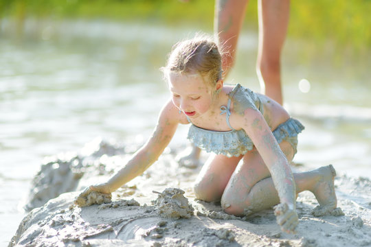 Young girl taking healing mud baths on lake Gela near Vilnius, Lithuania. Child having fun with mud. Kid playing with clay.