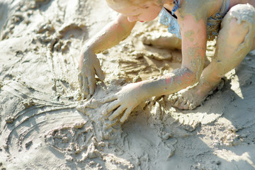 Obraz premium Young girl taking healing mud baths on lake Gela near Vilnius, Lithuania. Child having fun with mud. Kid playing with clay.