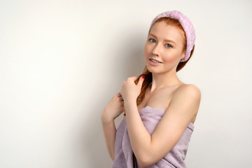 A red-haired girl in a lilac towel stands half-turned on a white background and looks at the camera, straightening hair