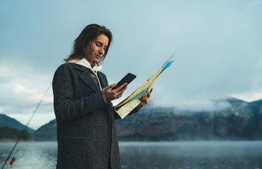 hipster tourist using smartphone planning trip with map on foggy lake, mist in mountain nature, traveler look landscape vacation trip, enjoy lifestyle holiday concept