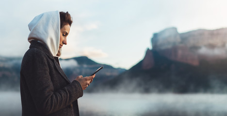 hipster tourist using smartphone planning trip on foggy lake, mist in mountain nature, traveler...