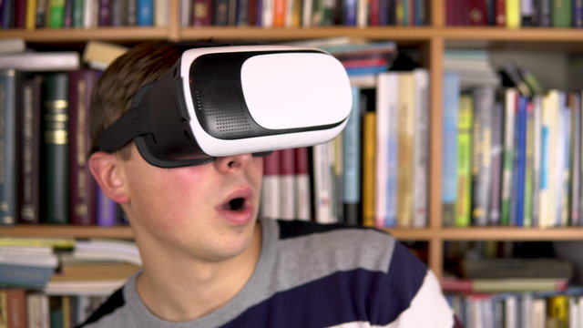 Young man in VR glasses in the library. A man with a VR helmet on his head. In the background are books on bookshelves. Book library.