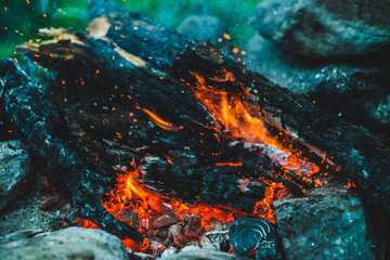 Fototapeta na wymiar Vivid smoldered firewoods burned in fire close-up. Atmospheric background with orange flame of campfire. Full frame image of bonfire. Warm whirlwind of glowing embers and ashes in air. Sparks in bokeh