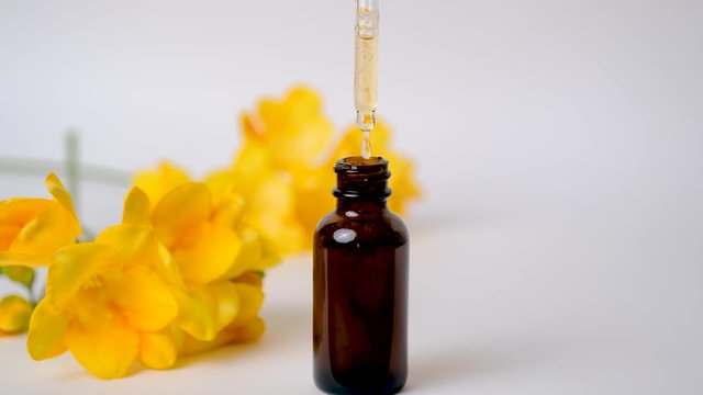 Close up of hand of young woman opening dark brawn bottle with hyaluronic acid, cosmetic serum. Drops of essential oil falls from cosmetic pipette into container on blurred yellow spring flowers.