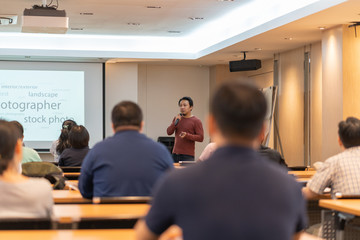 Asian Speaker is speaking on the stage over the presentation screen in the education seminar