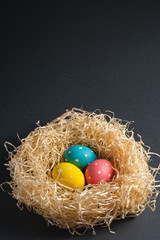 Colorful polka dot Easter eggs in wooden nest on dark grey black plain background, greeting card, copy space, angle view