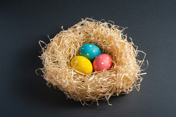 Colorful polka dot Easter eggs in wooden nest on dark grey black plain background, greeting card, copy space, angle view