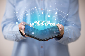 Businessman holding a foldable smartphone with SOFTWARE IMPLEMENTATION inscription, new technology concept