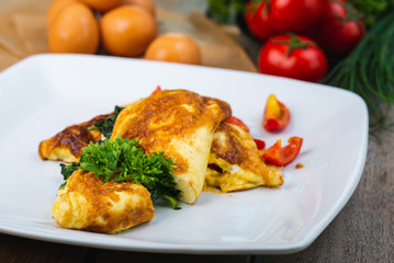 Traditional omelet with vegetables, spinach, tomatoes and herbs on a wooden table in a restaurant.