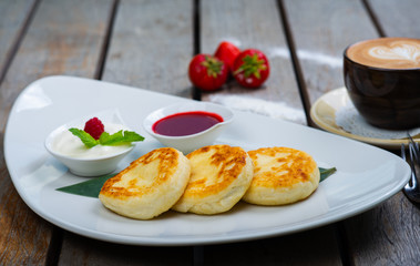 Traditional breakfast with coffee and cheesecakes, cottage cheese pancakes on a plate with syrup and jam.