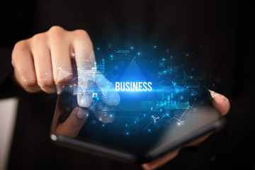 Businessman holding a foldable smartphone with BUSINESS inscription, business concept