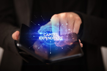 Fototapeta na wymiar Businessman holding a foldable smartphone with CAPITAL EXPENDITURE inscription, new business concept