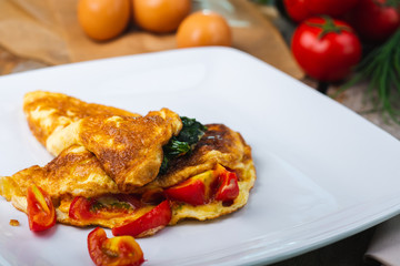 Traditional omelet with vegetables, spinach, tomatoes and herbs on a wooden table in a restaurant.