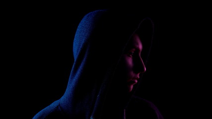 A young woman in a hood looks around. An attacker is standing in the dark. Blue and red light falls on a person on a black background.