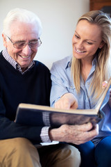 Grandfather Looking At Photo Album With Adult Granddaughter
