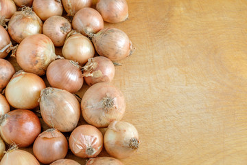 Yellow onions lie on the left on a wooden table.