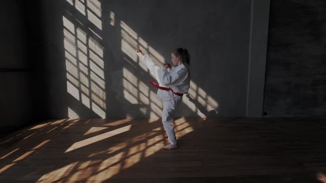 The girl shows a kick attack in traditional taekwondo. Original martial arts of south korea. Combat stance. Barefoot, sun grid, sport hall. General view.