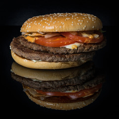 twisted fresh tasty burger on a black mirror surface with reflections isolated on black background